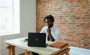 A smiling woman working on a laptop in a bright office environment.